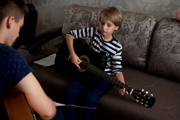 Un jeune musicien apprend à un petit garçon à jouer de la guitare acoustique et à jouer par notes — Photo