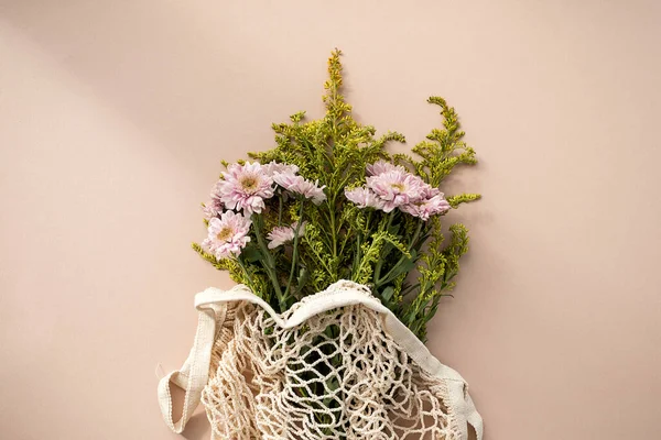 Draufsicht schöner Strauß rosa Chrysanthemenblüten in einer Netztasche auf blassrosa beigem Hintergrund. — Stockfoto