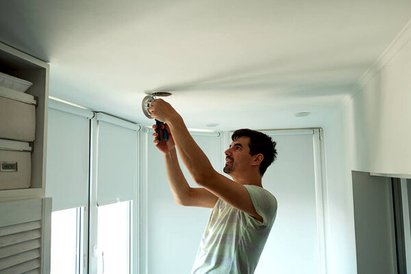 House master male electrician repairs ceiling light indoor home in white room