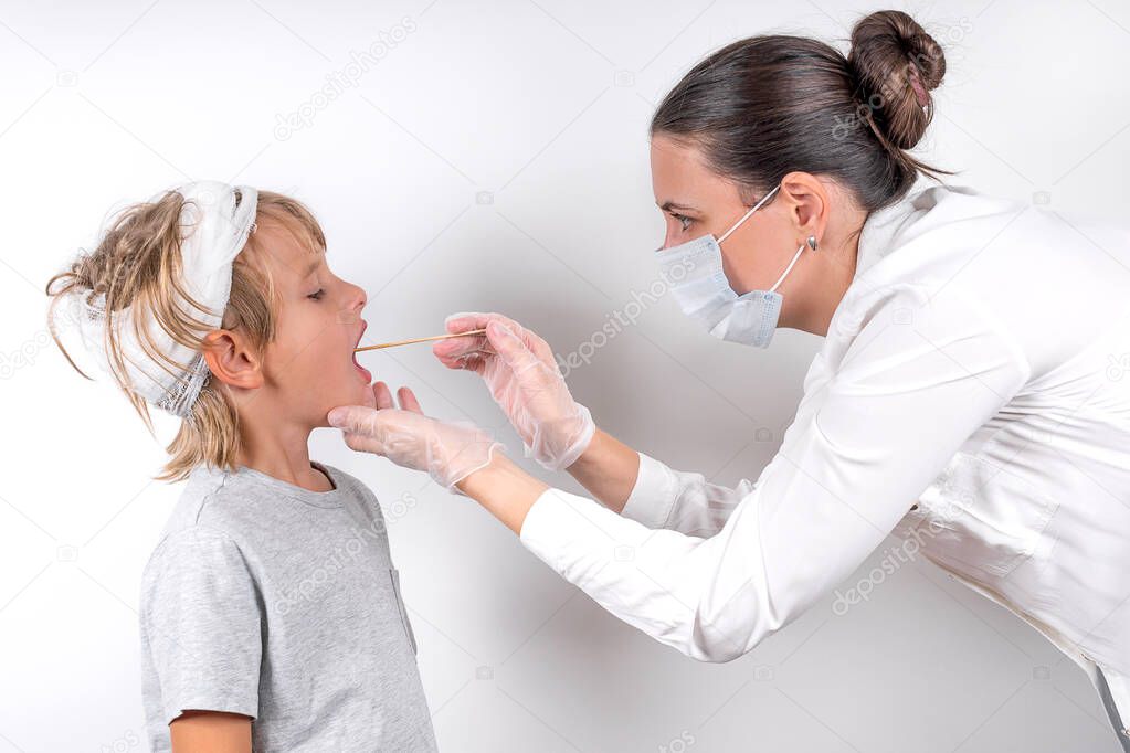 Medicine, healthcare and pediatry concept. A female doctor in medical mask and transparent gloves examines a sick little boy with head injury. Checks the throat and takes a swab for the coronavirus.