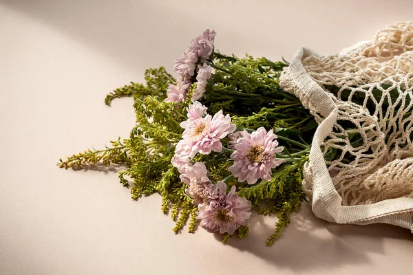 Mooi boeket van roze chrysant bloemen in een mesh zak op lichtroze beige achtergrond. — Stockfoto