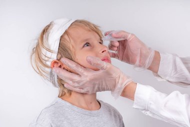 Kadın eli optometrist şeffaf tıbbi eldiven takıyor göz damlası gibi küçük sarışın çocuk gözlerini göz doktoru kliniğine koyuyor. İğrenç bir bakış. Beyaz arkaplan.