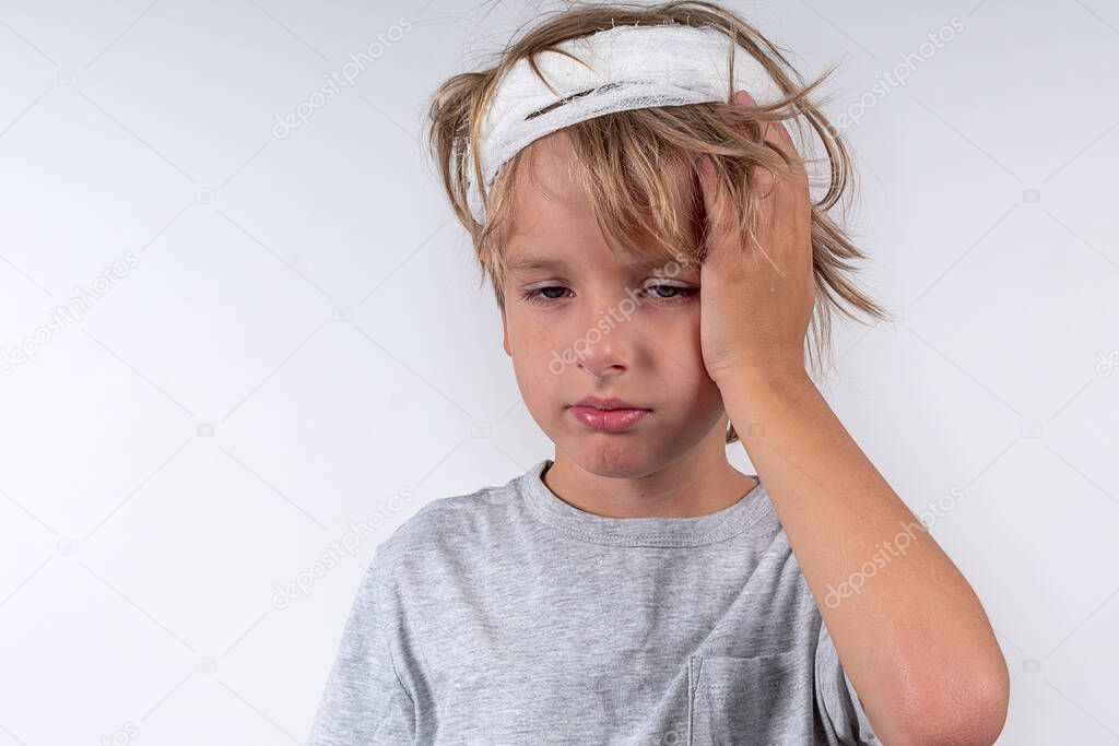 Portrait young caucasian cute boy blond hair with trauma injury and bandage head. Isolated on white background. Boy holds his head with his hand.