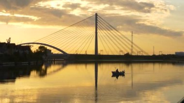 Gün batımında Gdask 'taki Martwa Wisa üzerinde asma köprü ve küçük bir teknede bir balıkçı. Güzel ışıkla kaplanmış serin bir atmosfer.