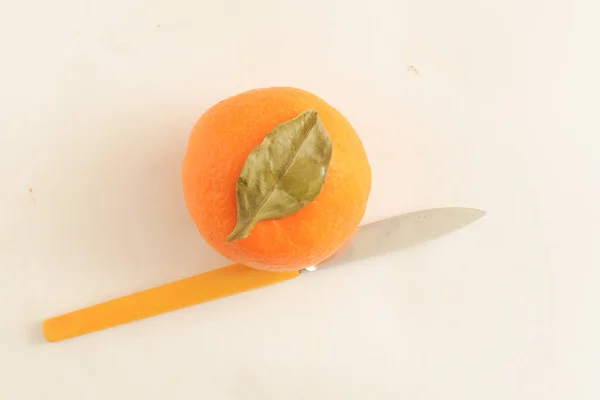 Vue de dessus, une mandarine entière avec feuille verte et un couteau pour couper. — Photo