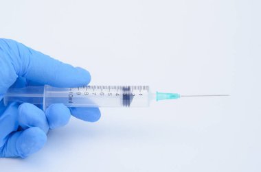 Doktorun elinde beyaz arka planda aşı için tek kullanımlık şırınga var..