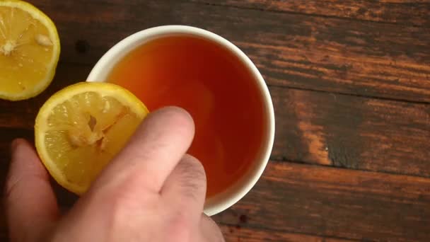 Muž hodí plátek citronu do šálku čaje na dřevěném pozadí — Stock video
