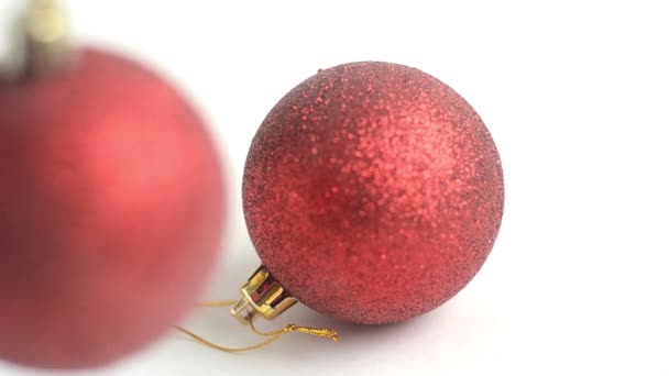 Yksi punainen joulupallo makaa valkoisella taustalla ja yksi punainen pallo heiluu epätarkkana. — kuvapankkivideo
