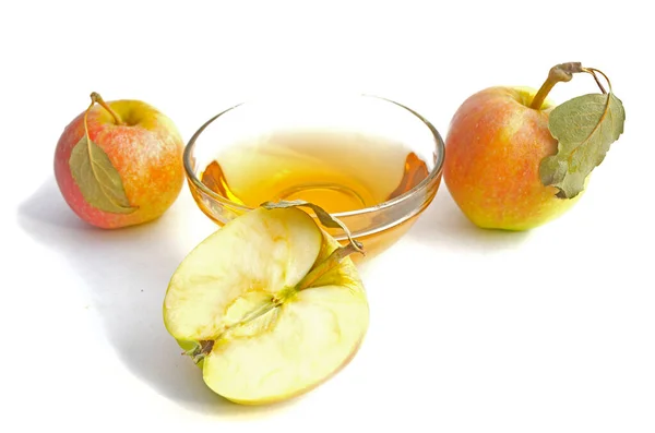 Dos manzanas con hojas, media manzana con hoja verde y un tazón con vinagre de sidra de manzana. — Foto de Stock