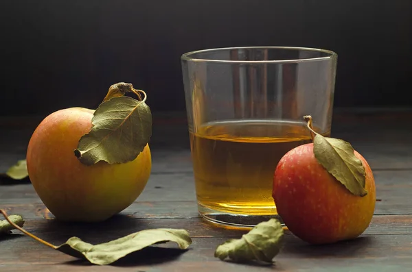 Un vaso con vinagre de manzana y dos manzanas con hojas sobre fondo de madera. — Foto de Stock