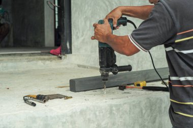 İnşaat alanındaki çimento zemininde sondaj makinesini tutan işçinin ellerine odaklanın.