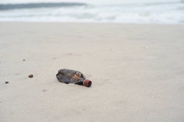 Arka planda bulanık deniz manzarası olan plajdaki plastik şişeye odaklan. Çöp ve çöp.