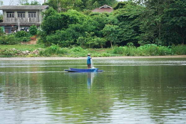 Lonely man stands on the boat and collects the fish from the net with forest in background.