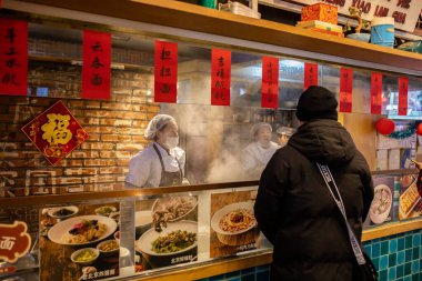 Çin 'de sokak yemeği standında siparişini bekleyen bir adam var.