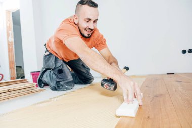 Gülümseyen erkek işçi inşaat alanına parke döşeme kuruyor. Parke döşeme  