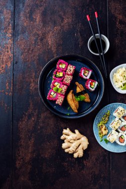 Lezzetli ruloların üst görüntüsü, suşi ve maki koyu ahşap bir tahta üzerinde yemek çubukları ile siyah kırsal arka planda