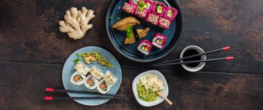 Lezzetli ruloların üst görüntüsü, suşi ve maki koyu ahşap bir tahta üzerinde yemek çubukları ile siyah kırsal arka planda