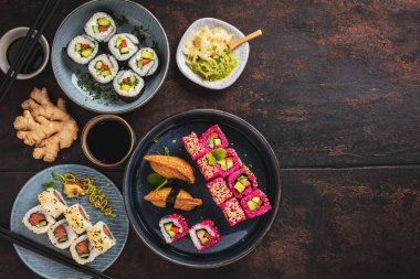 Lezzetli ruloların üst görüntüsü, suşi ve maki koyu ahşap bir tahta üzerinde yemek çubukları ile siyah kırsal arka planda