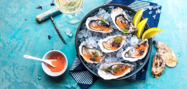 Mavi masada servis edilen limonlu, havyarlı ve buzlu lezzetli istiridye tabağının yakın görüntüsü..