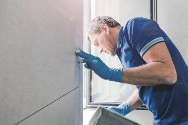 Ev tadilatı sırasında duvara fayans döşeyen orta yaşlı bir işçi.