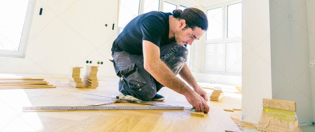 male worker varnishing oak parquet floor during home improvement