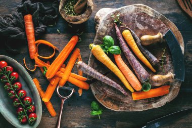 Tahta masadaki taze çiğ gökkuşağı havuçları ve otların yakın plan görüntüsü.