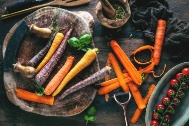 Tahta masadaki taze havuç, domates ve otların üst görüntüsü. 