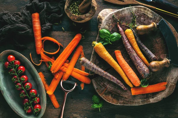 Tahta masadaki taze çiğ gökkuşağı havuçları ve otların yakın plan görüntüsü.