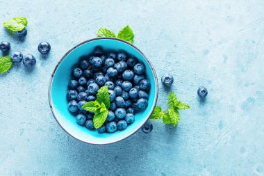 Mavi zemin üzerinde nane yaprakları olan taze olgun yaban mersinlerinin yakın plan görüntüsü