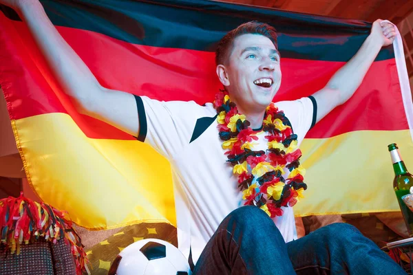 German football fan holding flag and watching the championship game on TV alone at home