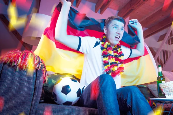 German football fan holding flag and watching the championship game on TV alone at home