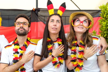 Bir grup coşkulu Alman futbol fanatiği bahçede futbol maçı izliyor.