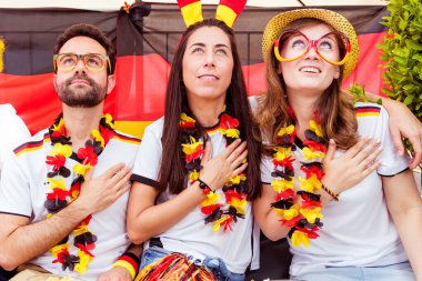 Bir grup coşkulu Alman futbol fanatiği bahçede futbol maçı izliyor.