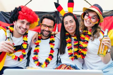 Bir grup coşkulu Alman futbol taraftarı bahçede dizüstü bilgisayarla futbol maçı izliyor.