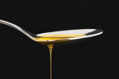 Siyah arka planda bir kaşıkta zeytinyağı damlası. Yemek pişirme