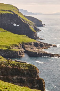 Faroe Adaları 'ndaki Atlantik uçurumlarında helikopter uçuyor. Danimarka