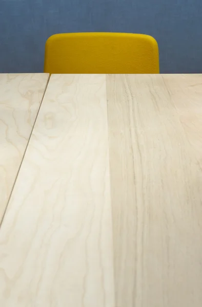 Wooden table and yellow chair over a blue wall — Stock Photo, Image