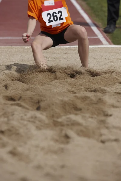 Hembra salto de longitud de la competencia con la mujer caer en la arena —  Fotos de Stock