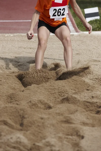 Hembra salto de longitud de la competencia con la mujer cayendo en la arena —  Fotos de Stock