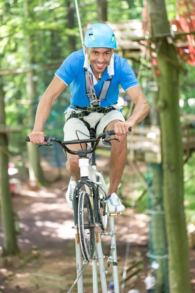 Homem anda de bicicleta na corda bamba em curso de corda alta — Fotografia de Stock