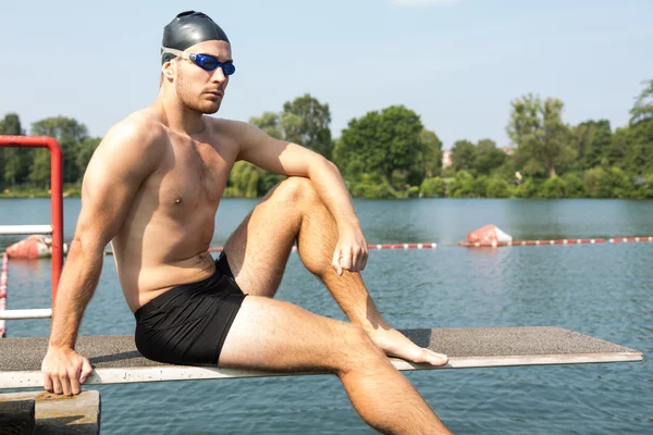 Man sitting on diving board in the sun at lake — Stock Photo, Image