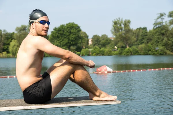 Man sitting on diving board in the sun at lake — Stock Photo, Image