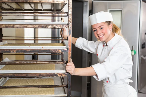 Ученик или работник в пекарне толкать стойку с тестом — стоковое фото