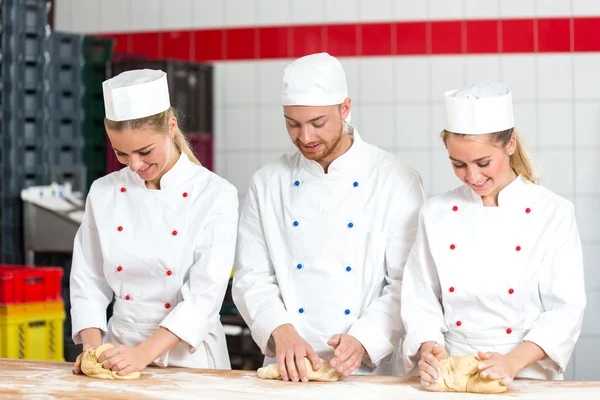 Three bakers in bakery kneading fresh dough — Stock Photo, Image