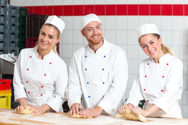 Three bakers in bakery kneading fresh dough — Stock Photo, Image