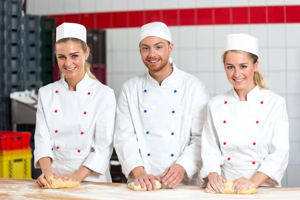 Tres panaderos en panadería amasando masa fresca —  Fotos de Stock