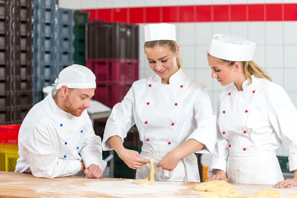 Leerling in bakkerij proberen te maken pretzels en sceptisch bakkers kijken — Stockfoto