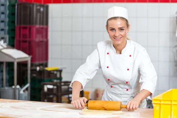Baker with dough roll working in a bakery — Stock Photo, Image