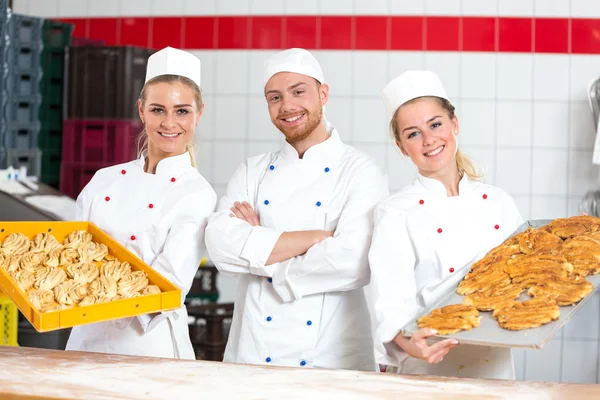 Bakkers in bakkerij poseren met bakken lade — Stockfoto