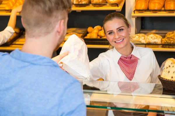 Winkelier in bakkerij de handzak van brood aan klant — Stockfoto